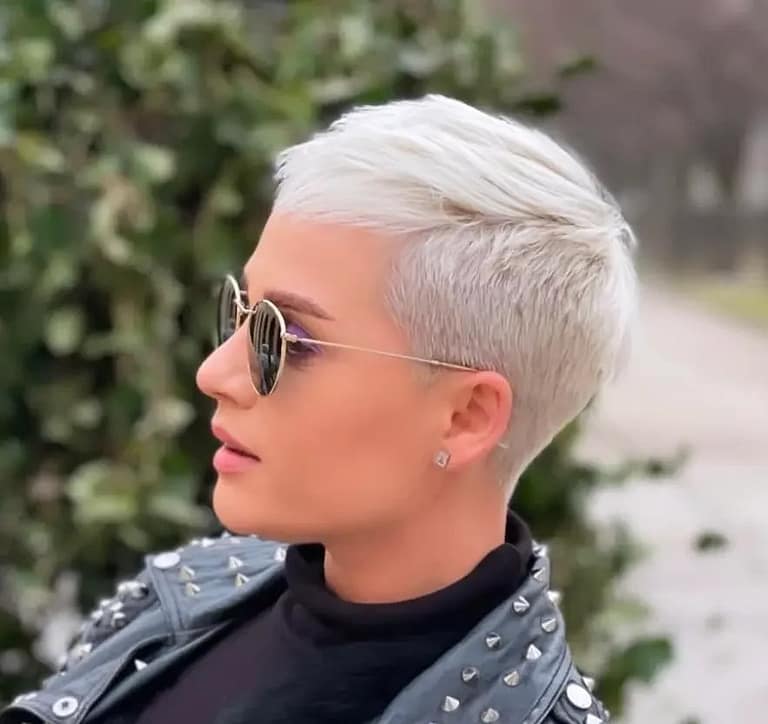 Stylish woman with a platinum blonde pixie cut wearing a studded leather jacket and sunglasses, exuding a bold and edgy look outdoors.